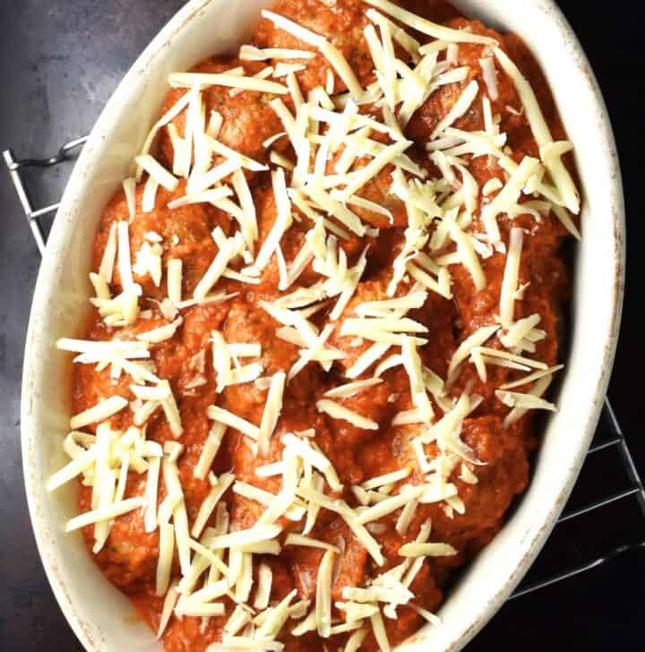 Quinoa turkey meatballs covered with sauce and shredded cheese in oval dish.
