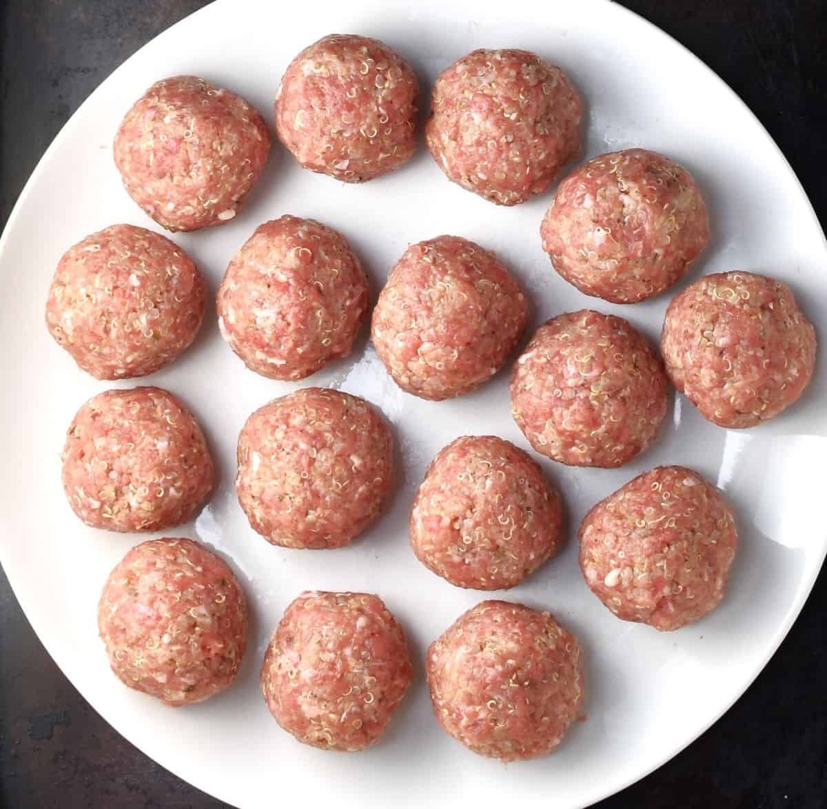 Raw turkey and quinoa meatballs on white plate.