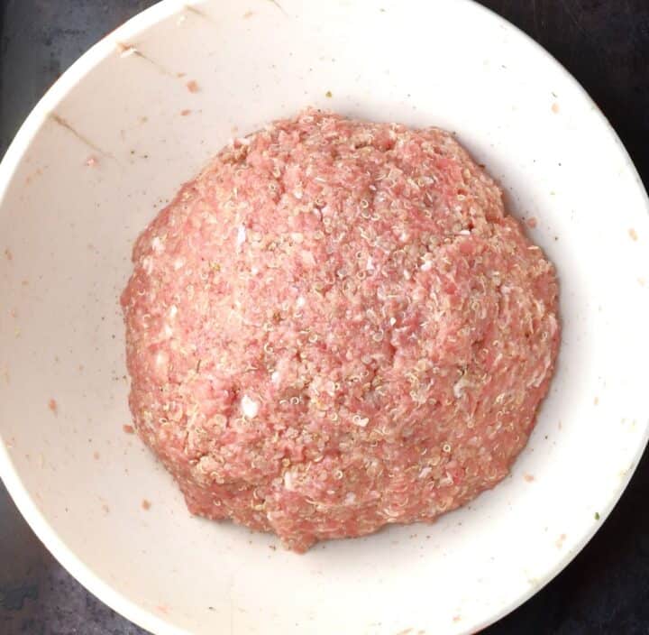Meatball mixture ball in white mixing bowl.