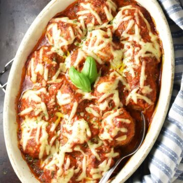 Top down view of turkey quinoa meatballs with sauce in oval dish.