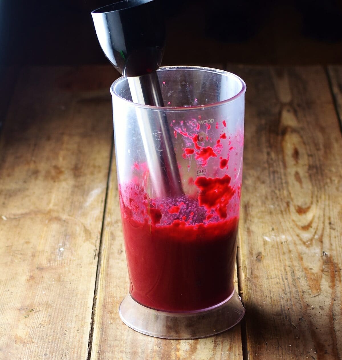 Beetroot puree in tall container with stick blender end inside.