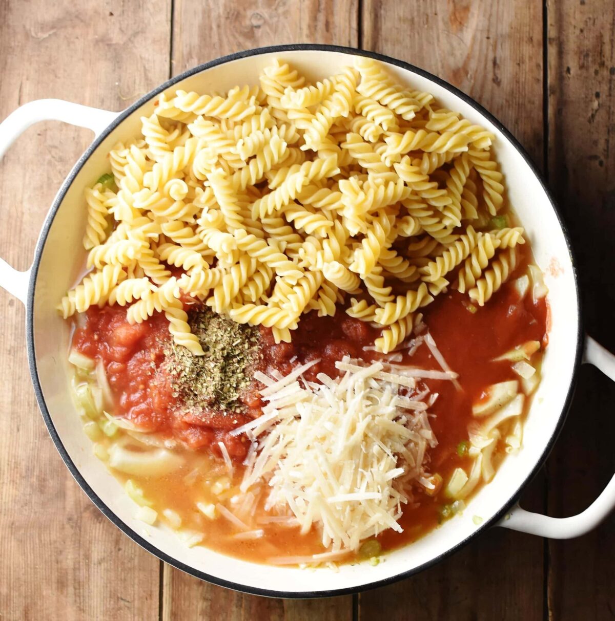 Fussili pasta, tomatoes, fennel and grated cheese in large white shallow dish.
