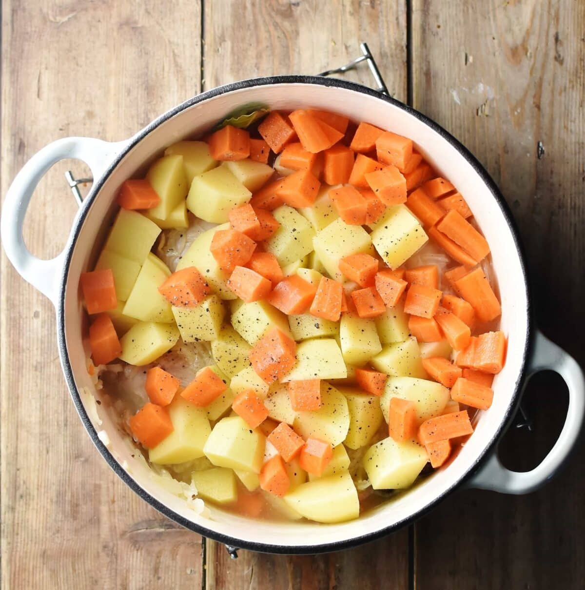 Cubed potatoes and carrots in large white pot.