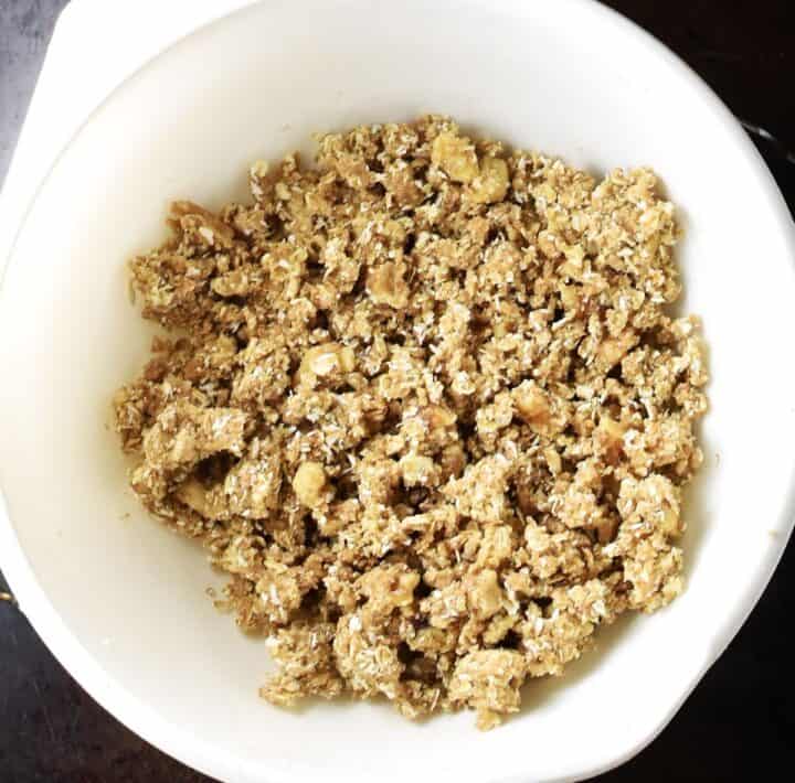 Top down view of crumble topping mixture for apple oat crumble in white bowl.