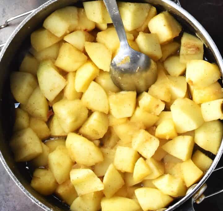 Top down view of cooked cubed apples for crumble with spoon in pot.