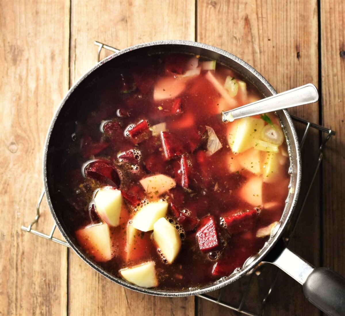Chopped beetroot, potatoes and stock in large pot with spoon.