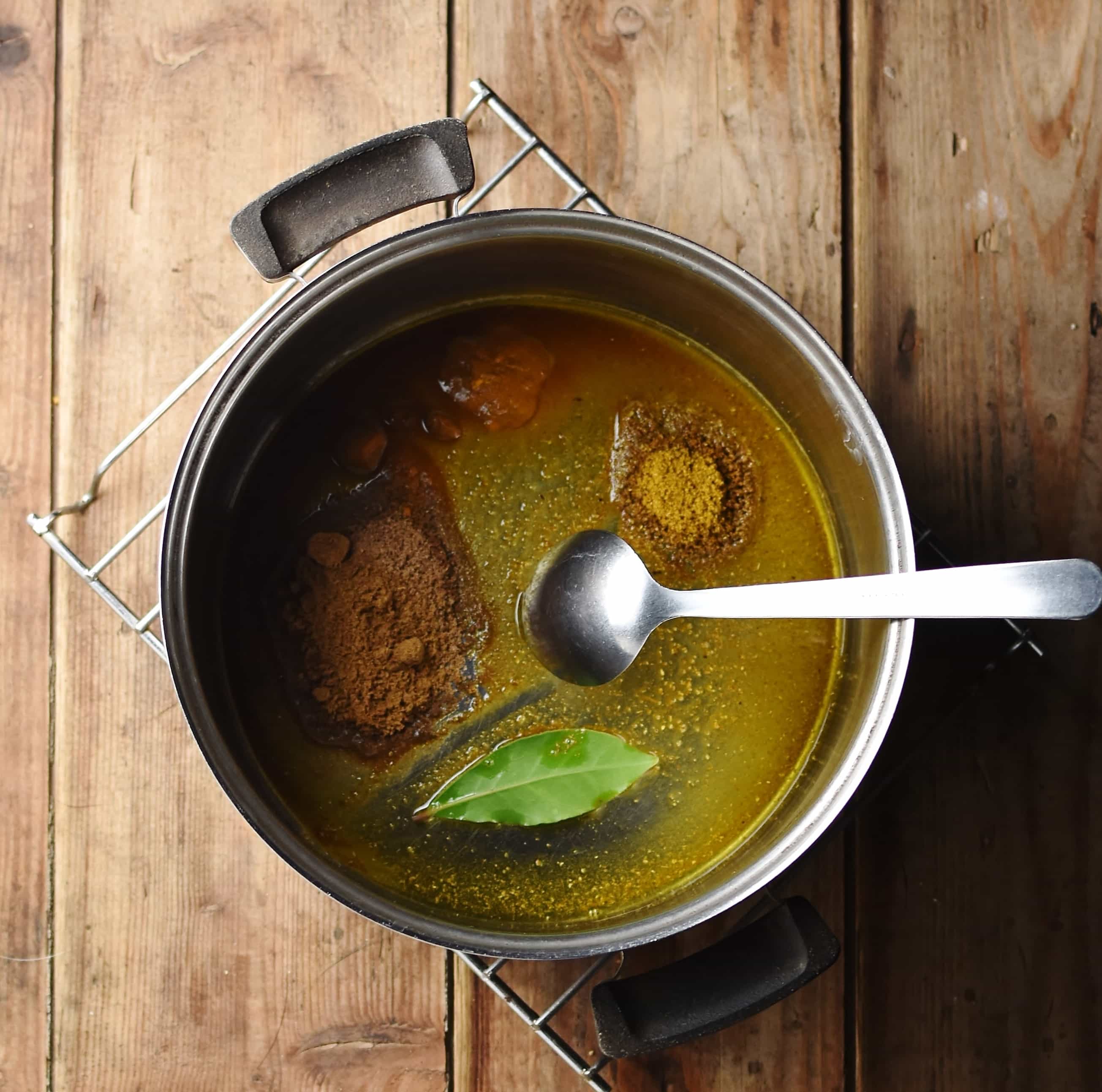 Spices with bay leaf and oil in pot with spoon.