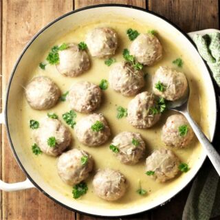 Meatballs in white sauce with spoon in large shallow dish.