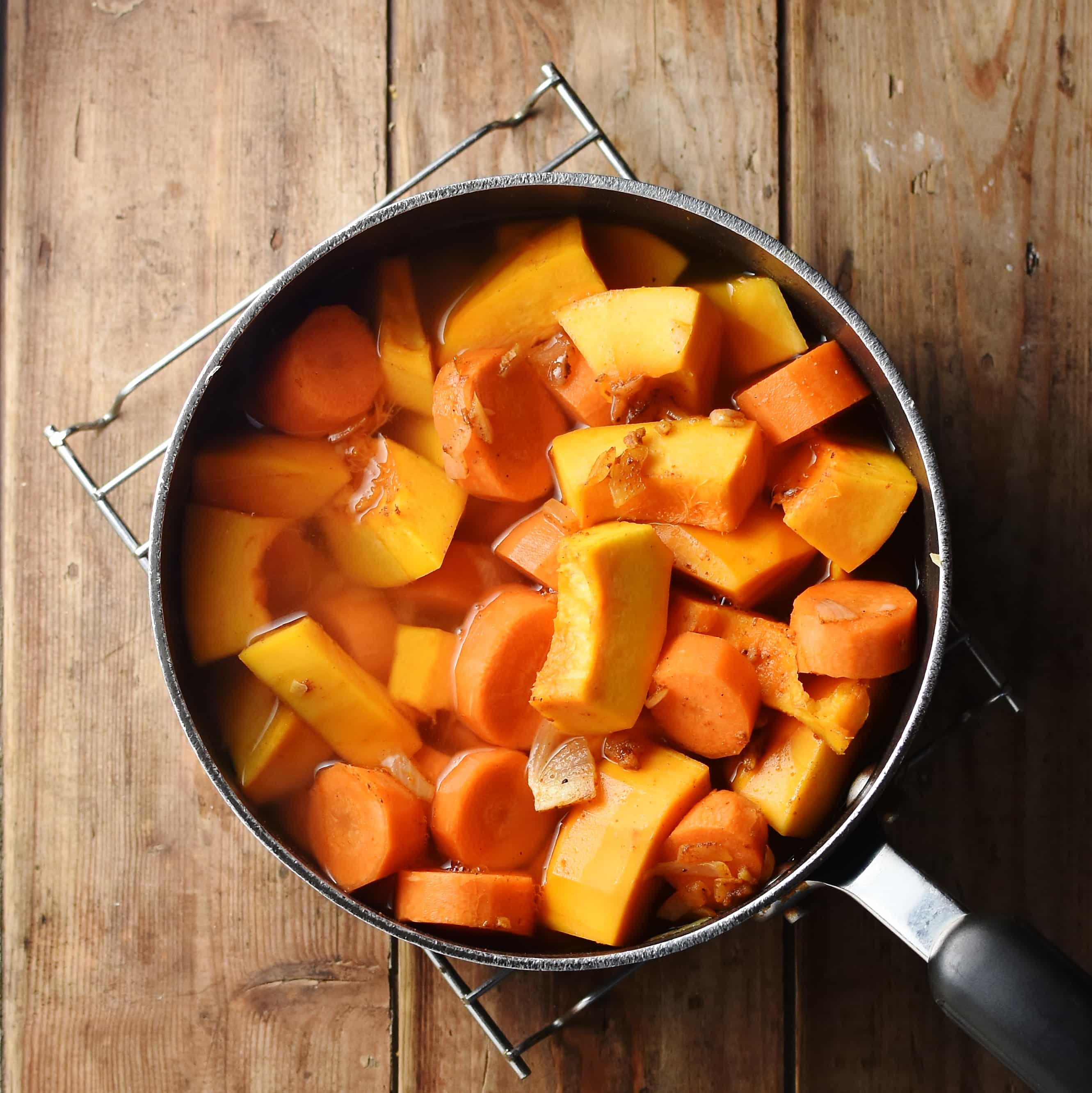 Chunks of pumpkin and carrot in pot with water.