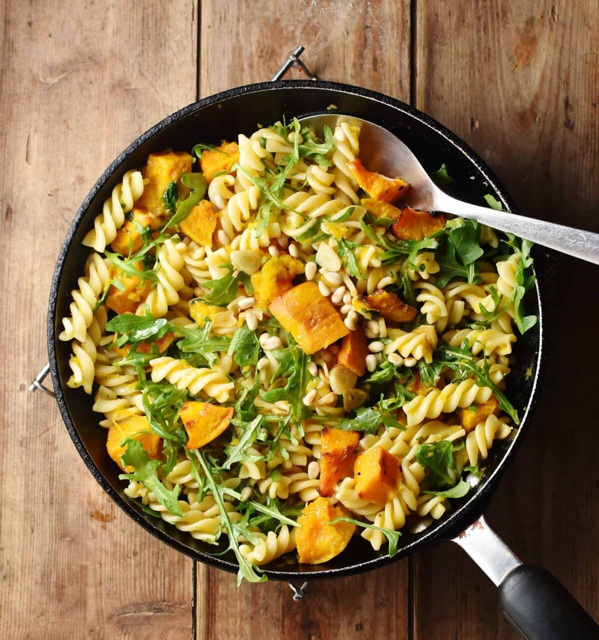 Pasta with pumpkin and arugula in pan with spoon.
