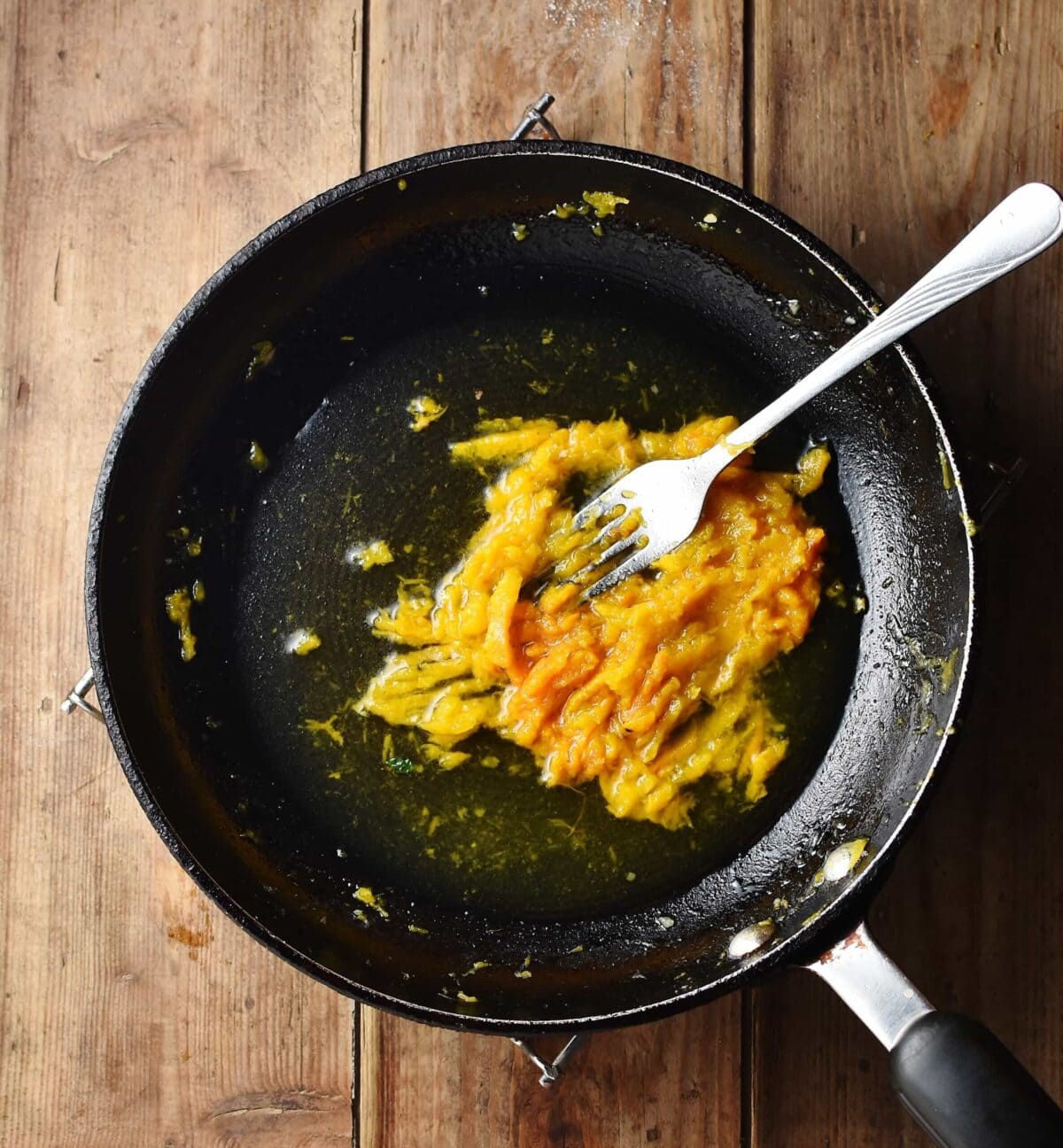 Mashed pumpkin with water and fork in black pan.