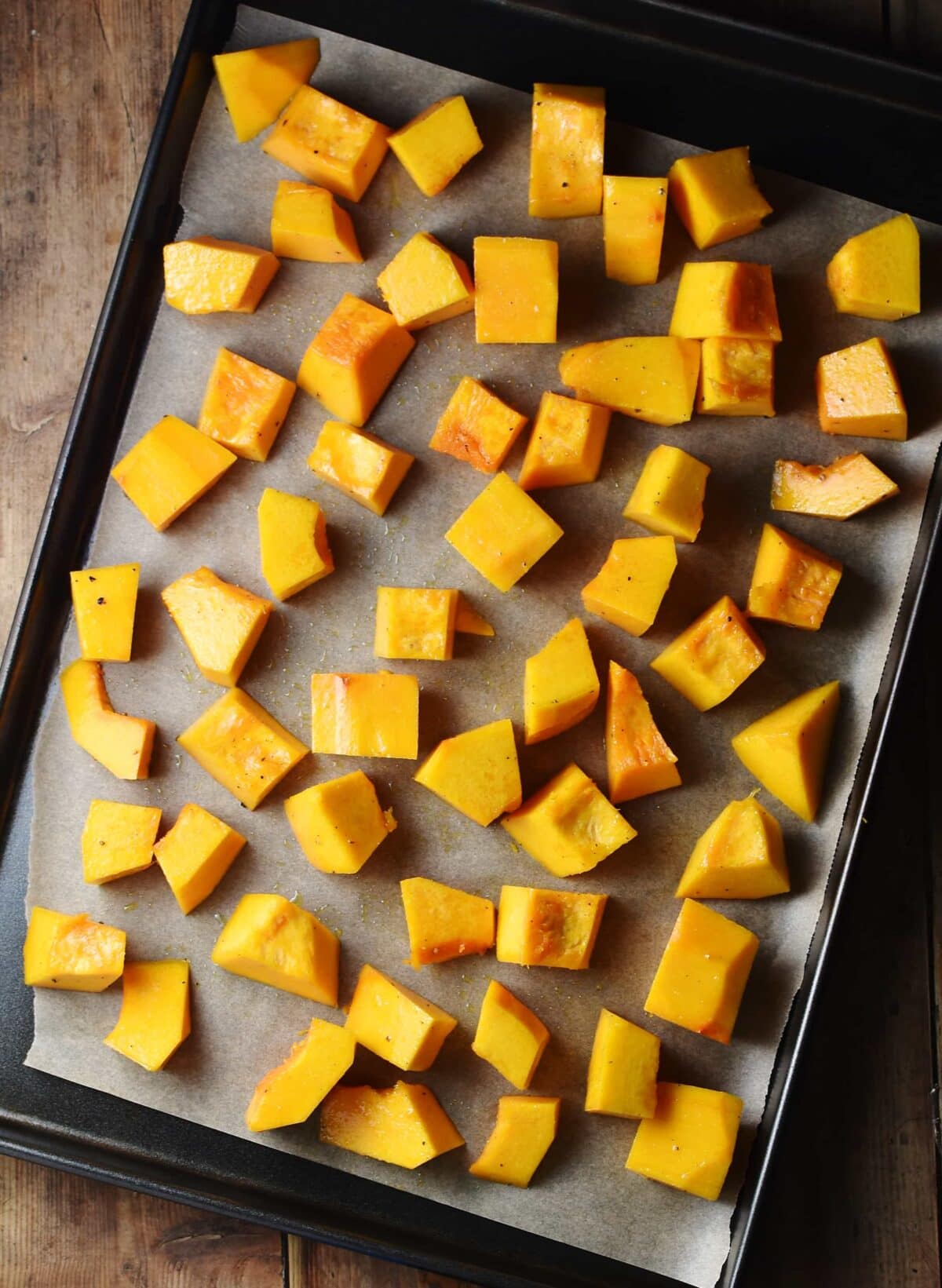 Cubed pumpkin on top of baking sheet lined with paper.