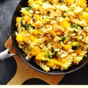 Pumpkin with pasta and herbs in skillet on top of cutting board.
