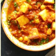 Top down close-up view of vegetable curry with paneer in white-and-yellow bowl.