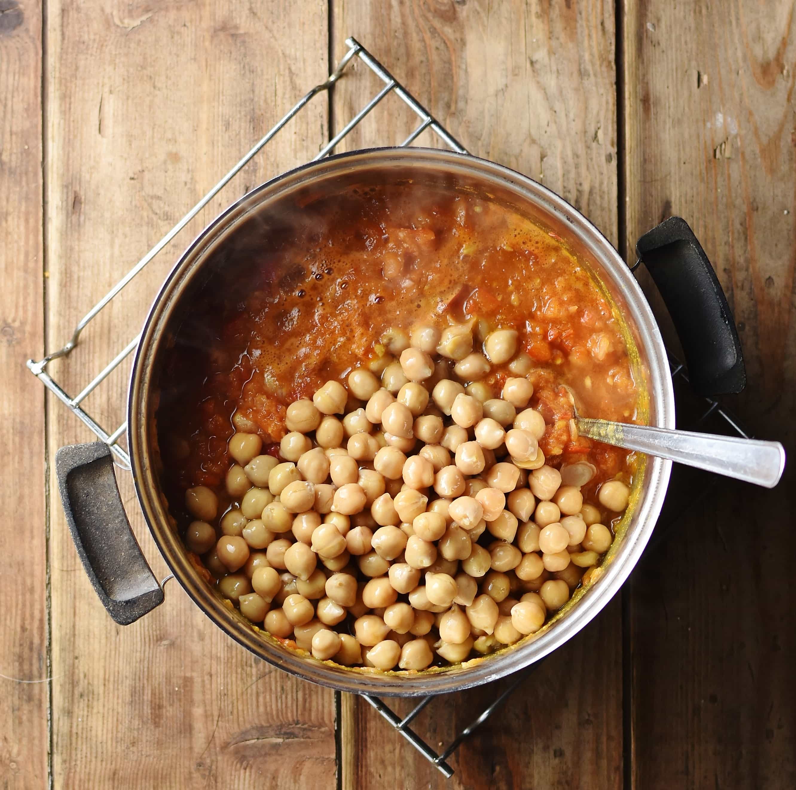 Chickpeas and tomato sauce in pot with spoon.