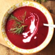 Top down view of beet fennel soup with cream in yellow bowl with with spoon.
