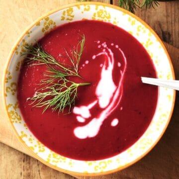 Top down view of beet fennel soup with cream in yellow bowl with with spoon.
