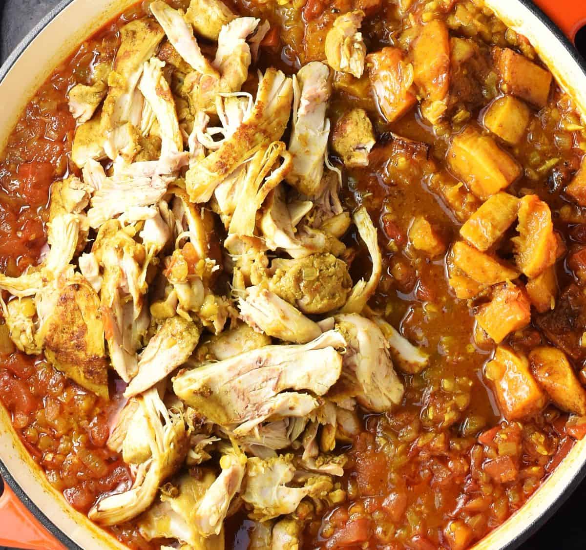 Top down view of chicken and butternut squash pieces added to curry sauce in large pan.