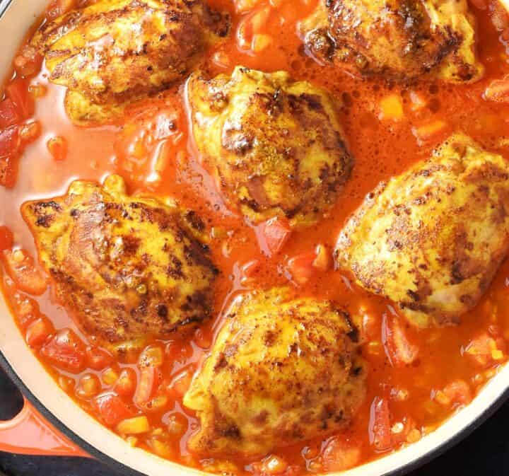 Cooking chicken thighs in curry sauce with lentil in large pan.