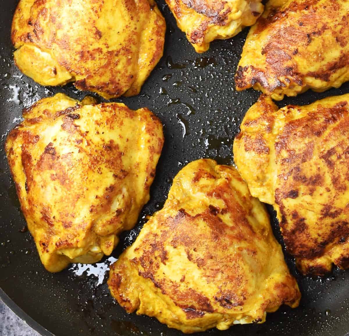 Top down view of browned chicken thighs in pan.