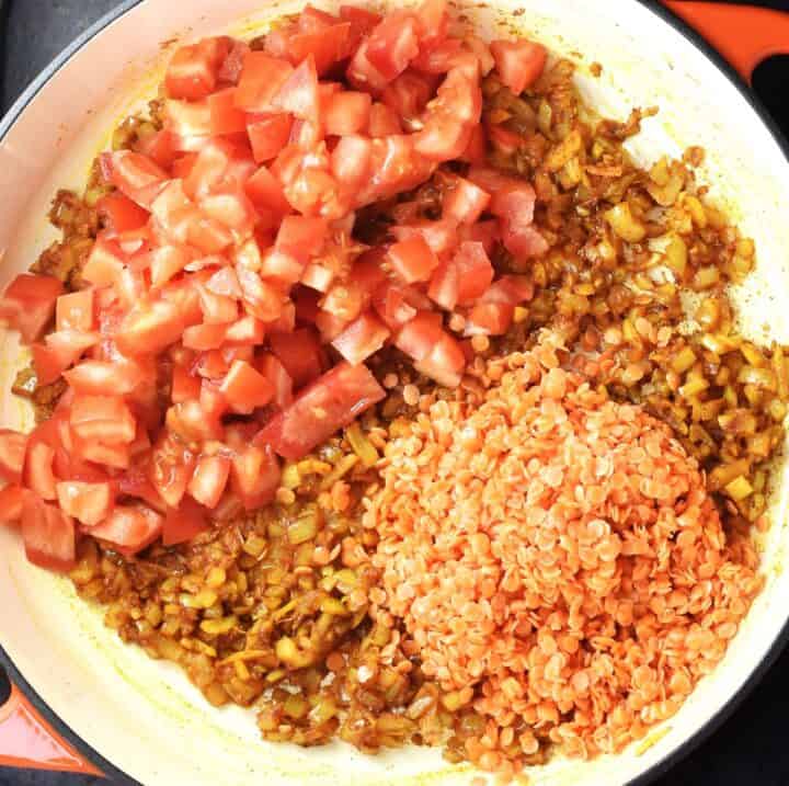 Chopped tomatoes and red lentils on top of fried onion in pan.