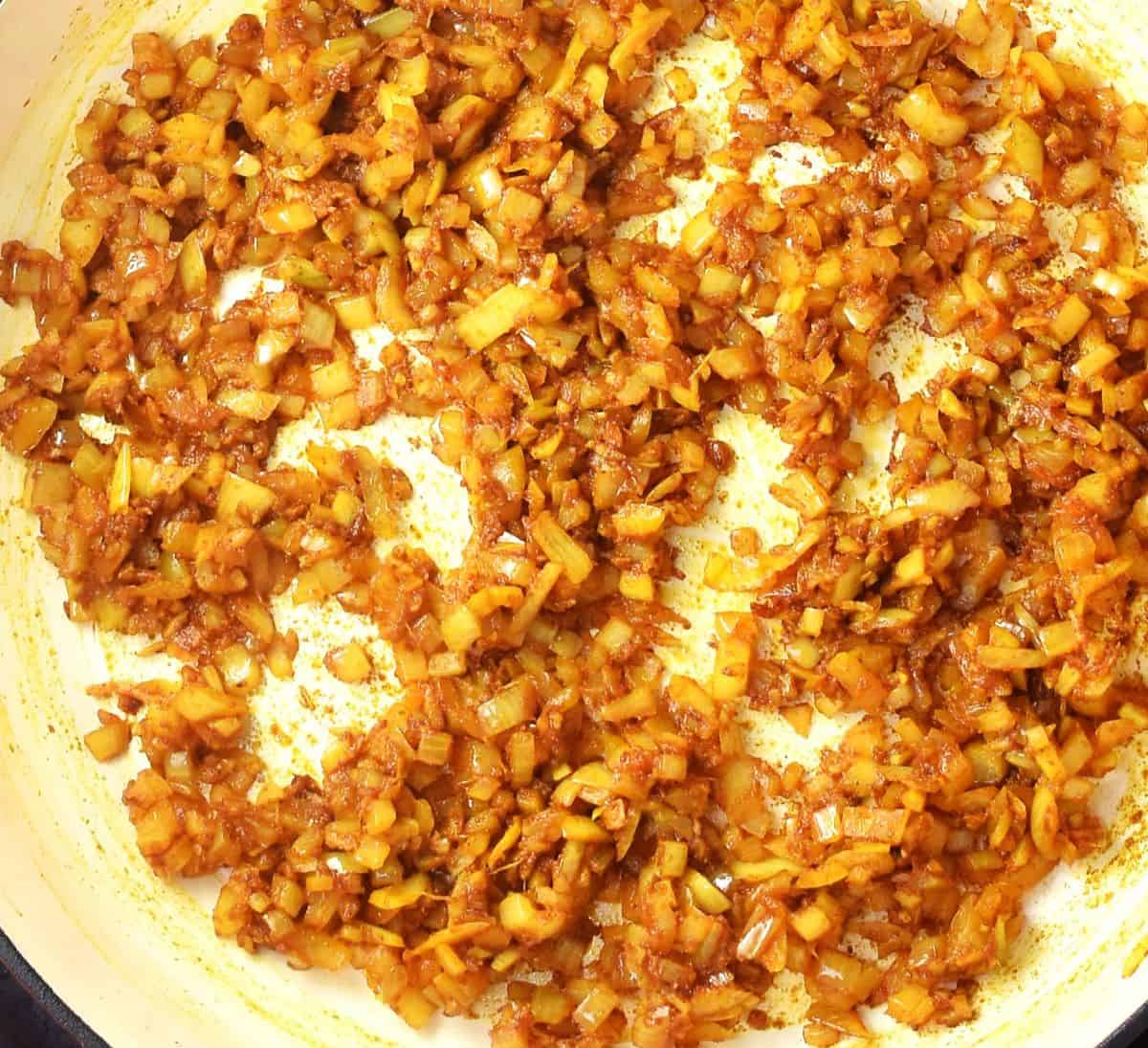 Top down view of chopped onions with spices in pan.