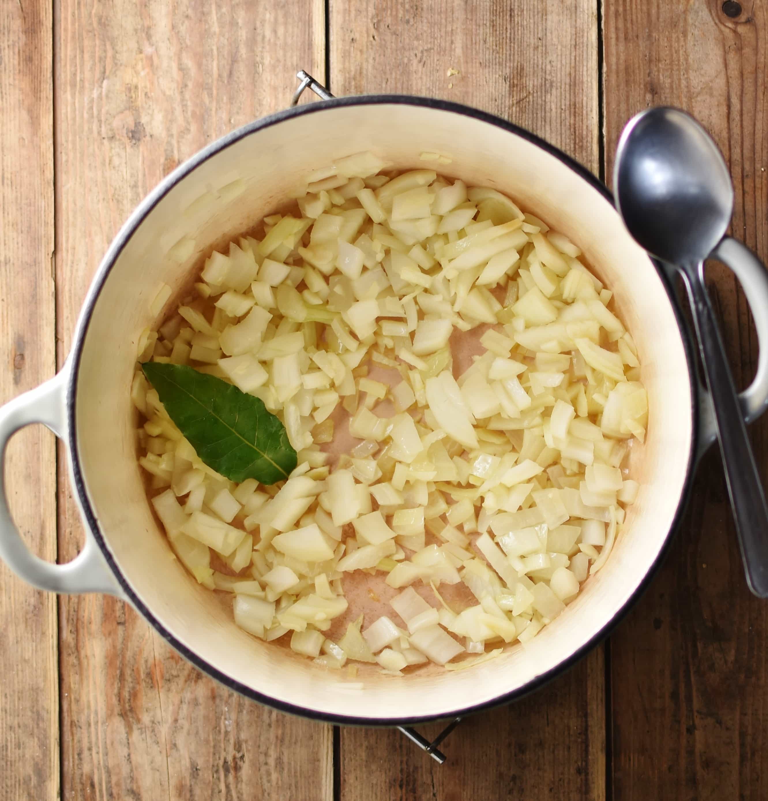 Fried onion with bay leaf inside white pot with spoon to the right.