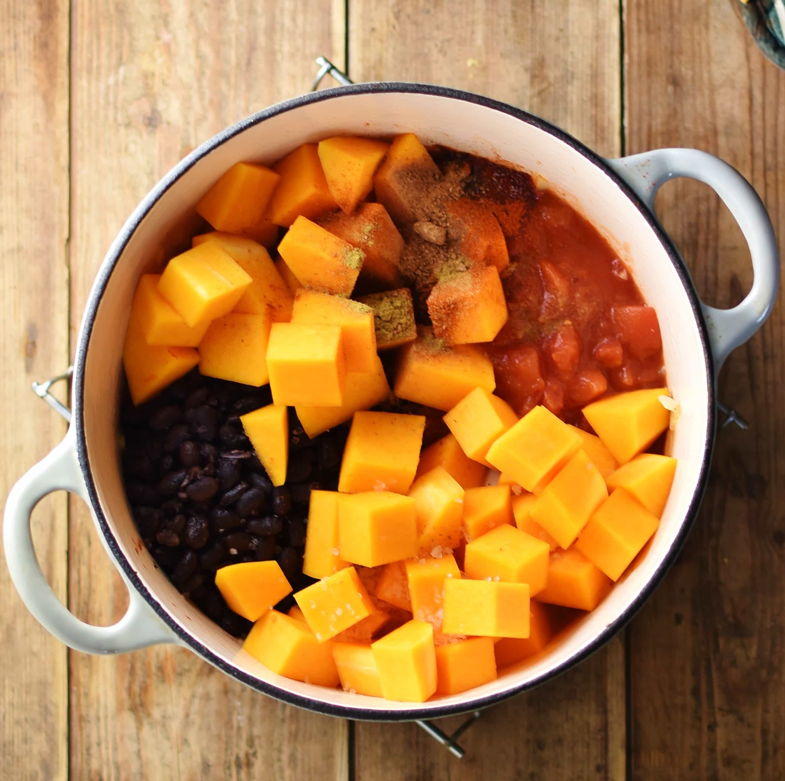 Cubed butternut squash, black beans, tomatoes and spices in white pot.