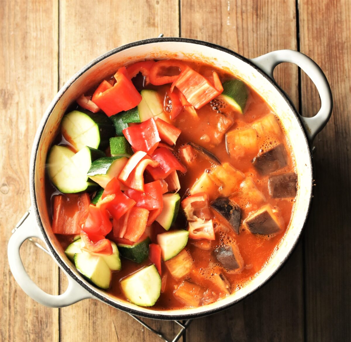 Chunky vegetables in tomato sauce in large white pot.