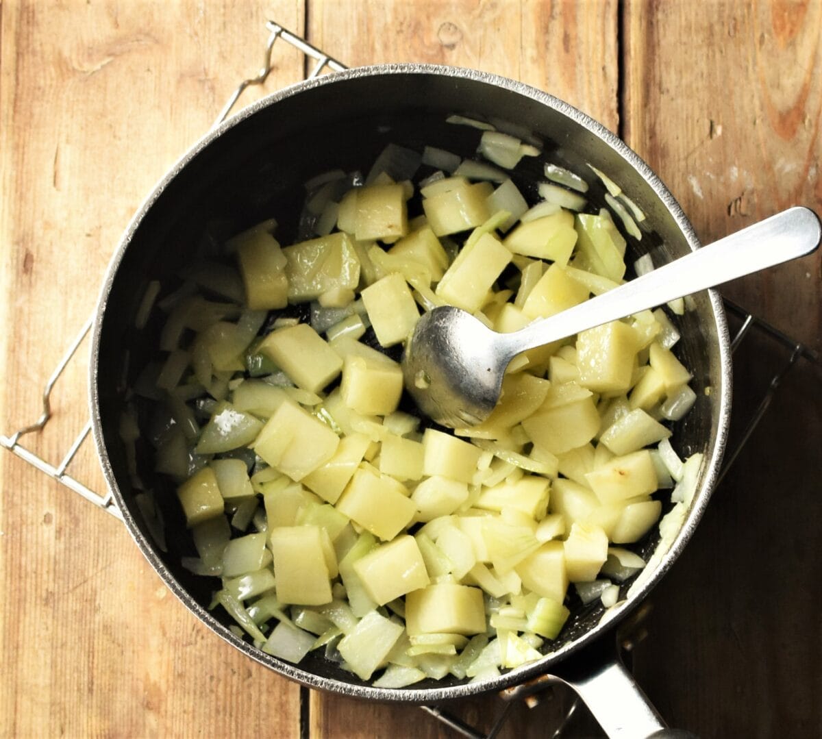 Cubed potatoes and chopped onion in large pot with spoon.