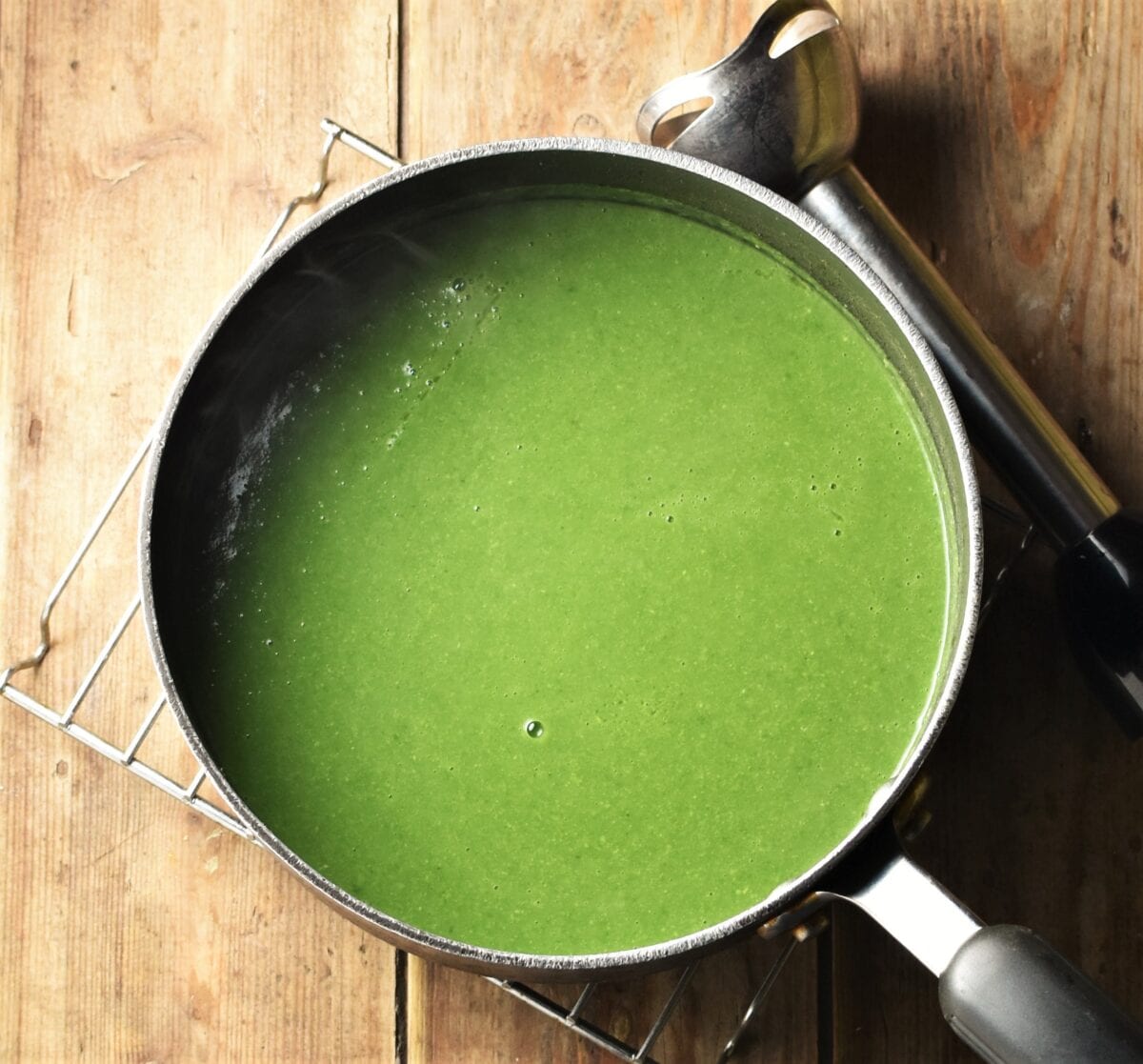 Pureed spinach and pea soup in large pot with hand blender in top right corner.