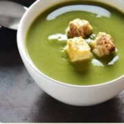 Pea soup with croutons in white bowl with lime in background.