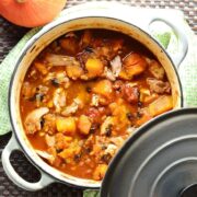 Chicken butternut squash casserole in white pot with grey lid on green cloth with squash.