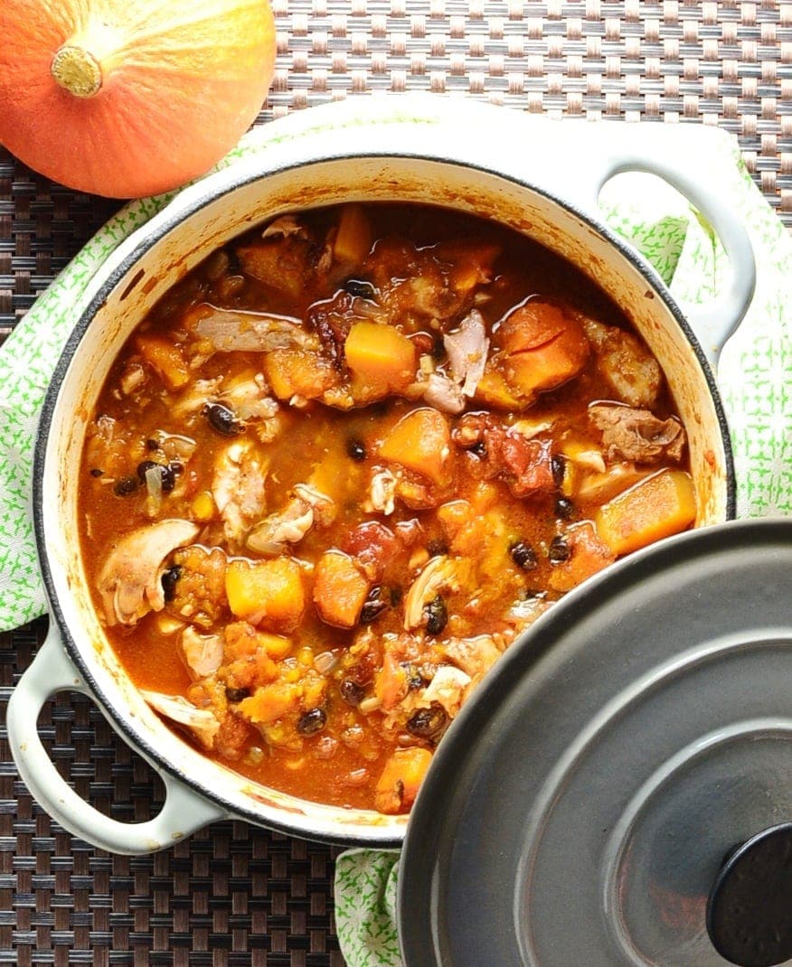 Chicken butternut squash casserole in white pot with grey lid on green cloth with squash.