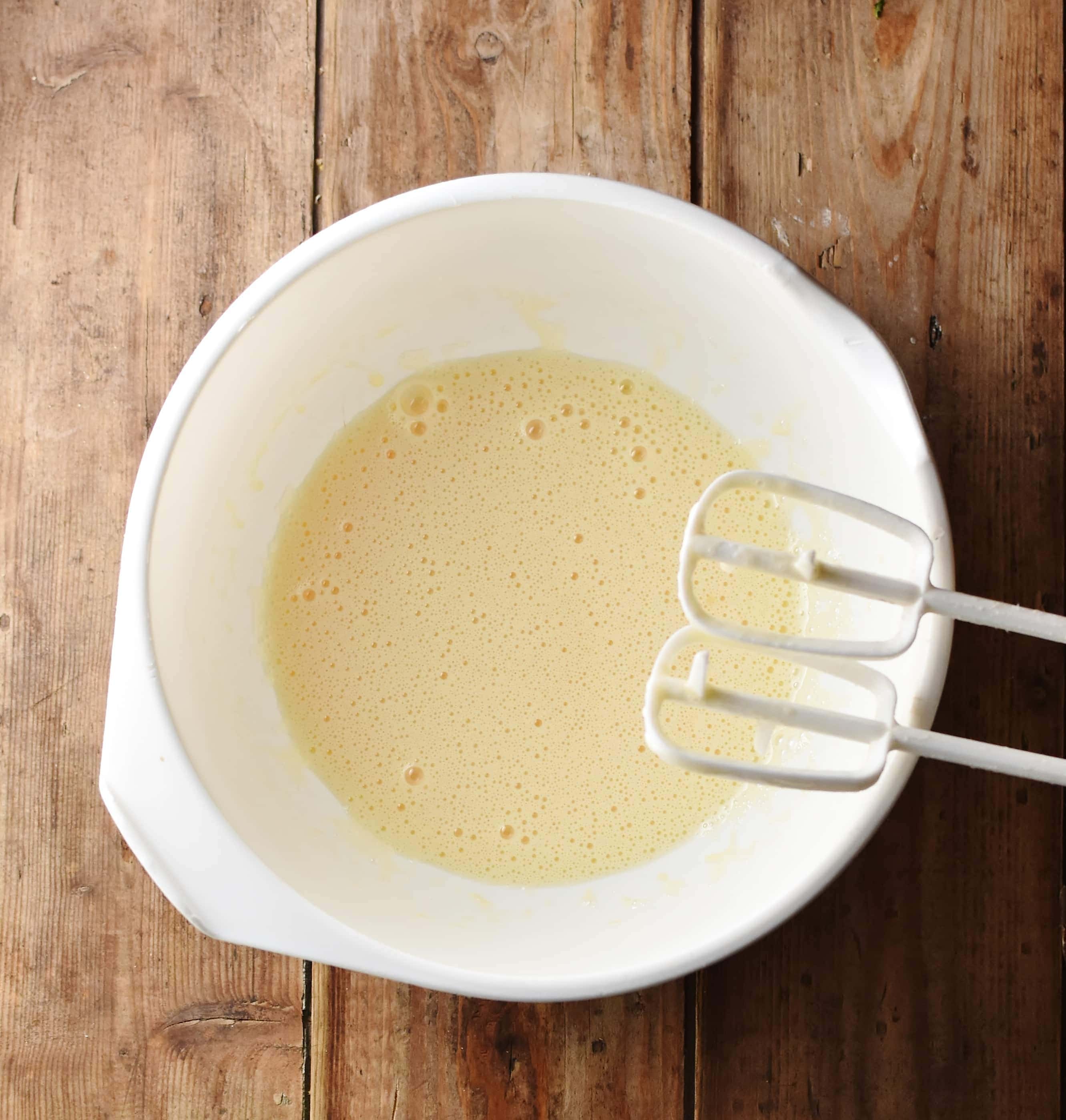 Smooth egg mixture in white bowl with ends of electric mixer visible.
