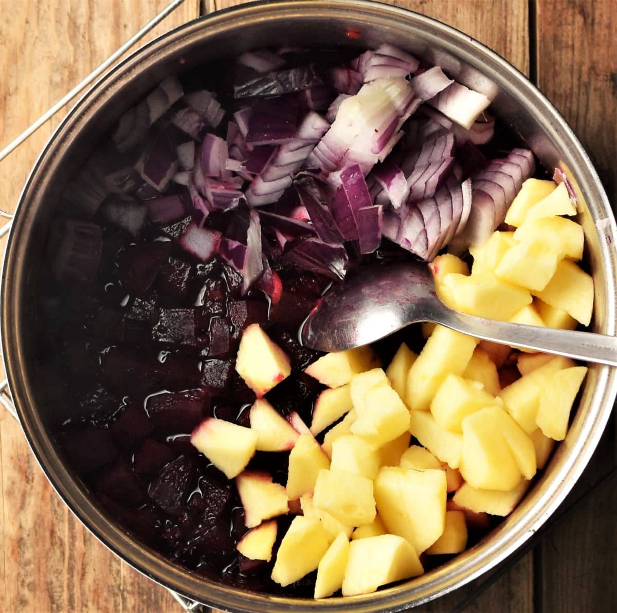 Cubed beets, apple, chopped red onion with spoon in pot.