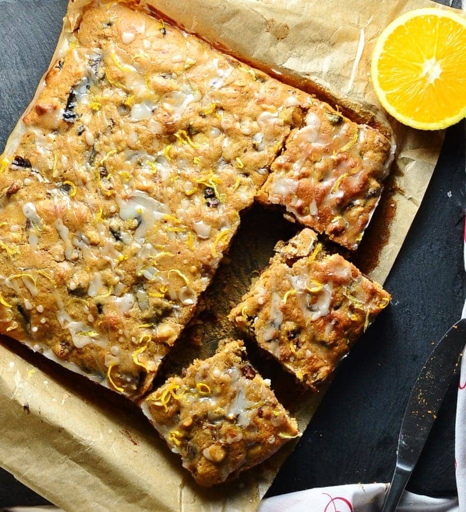 Top down view of fruit cake on top of parchment paper with halved orange and knife.