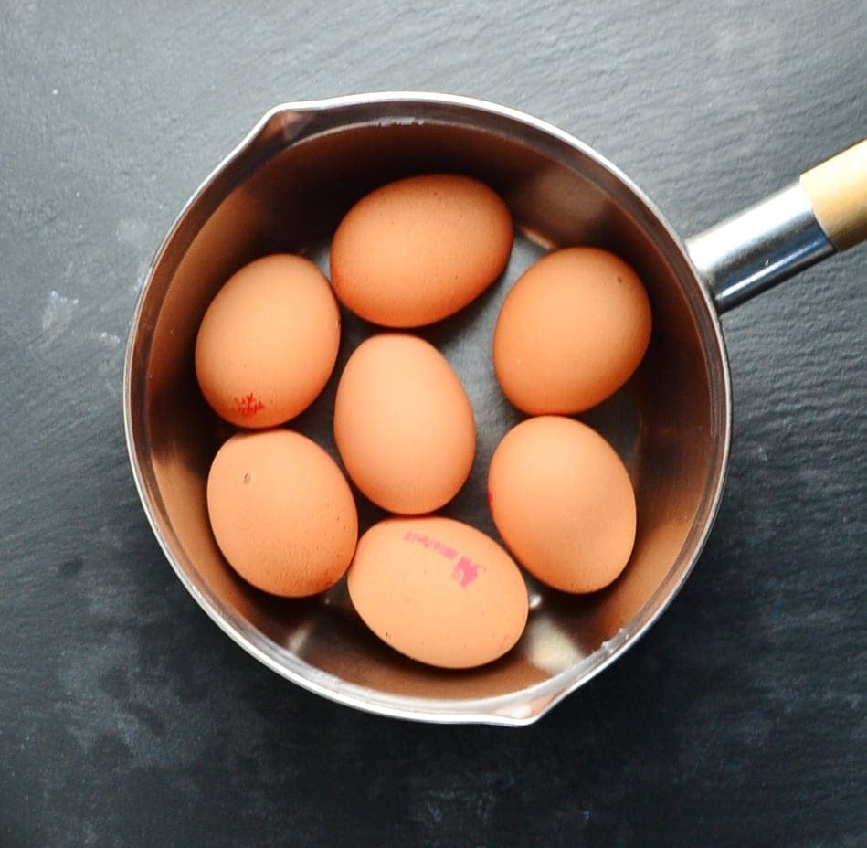 Top down view of 7 eggs in shells in saucepan on grey surface.