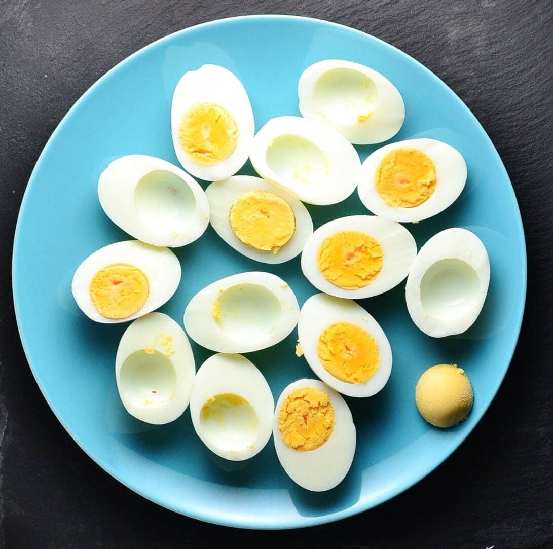 Top down view of hard boiled egg halves on blue plate on grey surface.