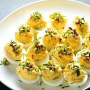 Smoked salmon deviled eggs with garnish of pistachios and chives on white plate.