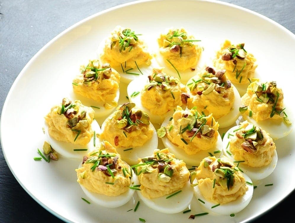 Smoked salmon deviled eggs with garnish of pistachios and chives on white plate.