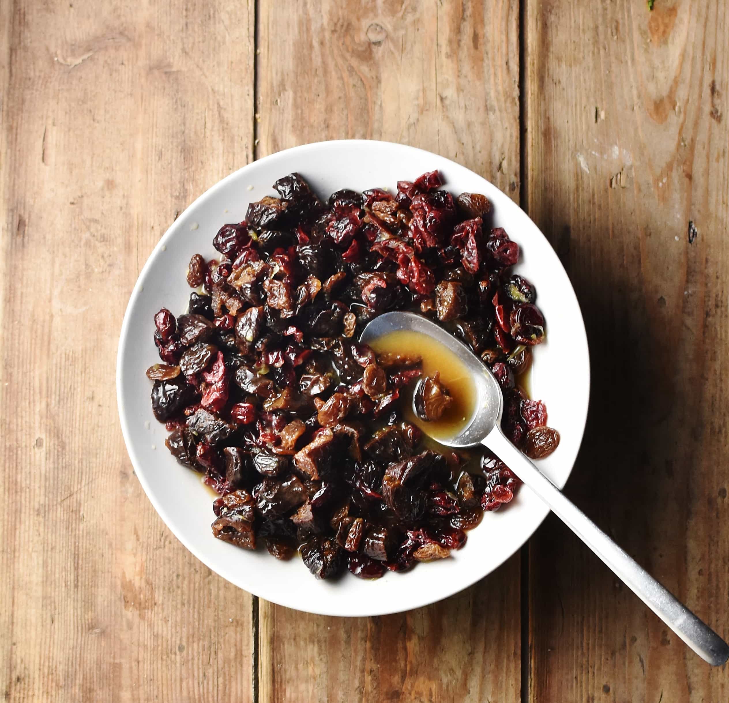 Mixed dried fruit in white bowl with spoon.