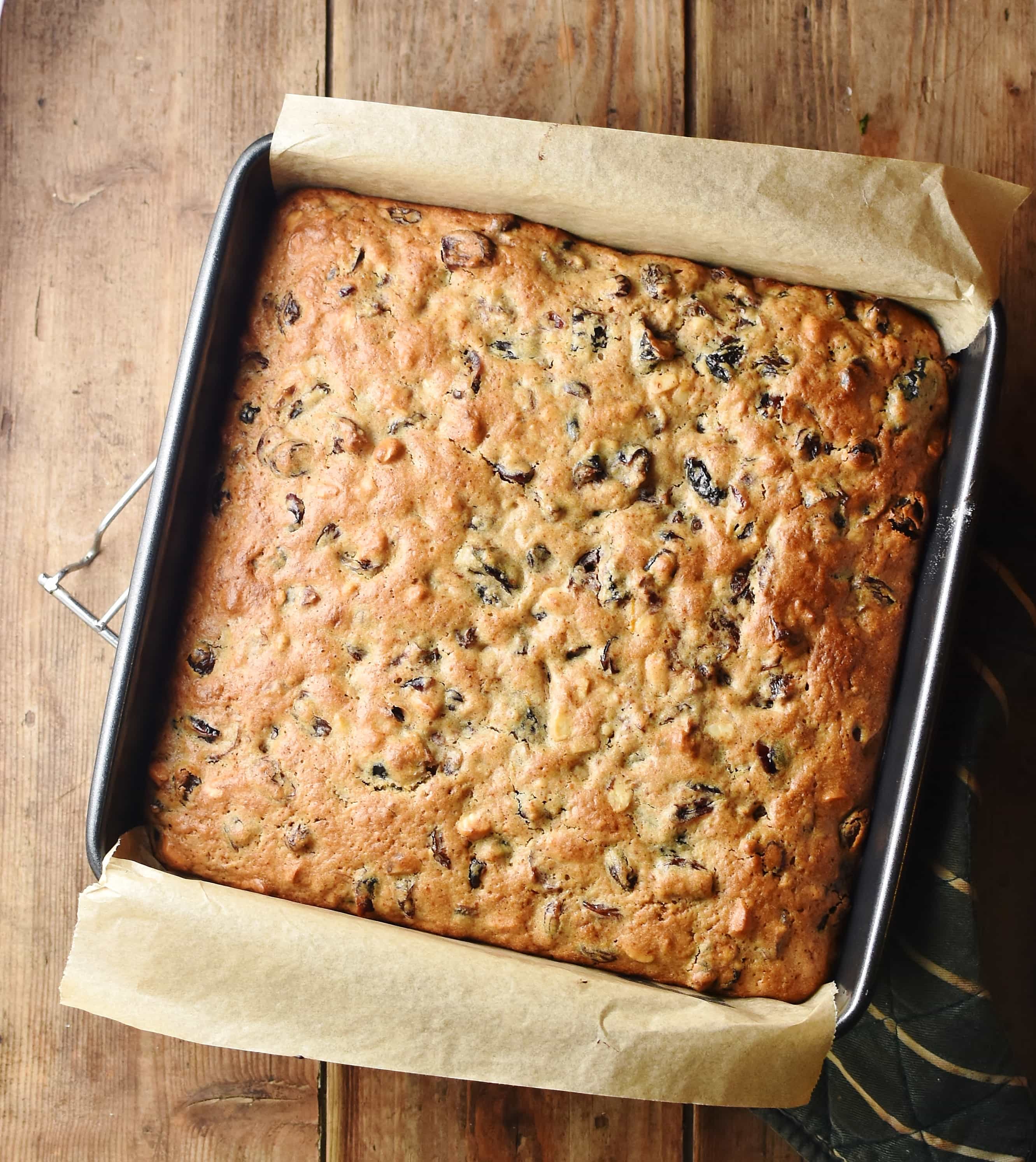 Top down view of baked fruit cake in square pan lined with paper.
