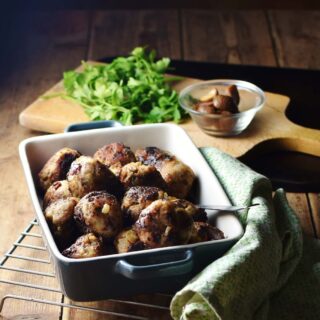 Stuffing meatballs in square blue dish with green cloth to the right, herbs and chestnuts in small dish in background.