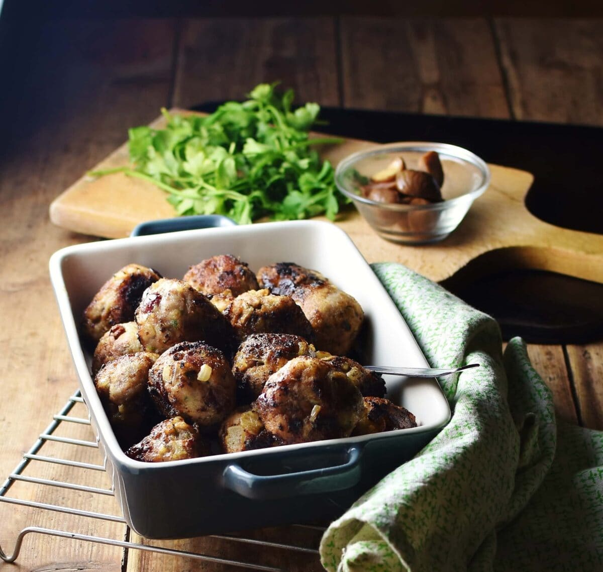 Stuffing balls in square blue dish with green cloth to the right, herbs and chestnuts in small dish in background.