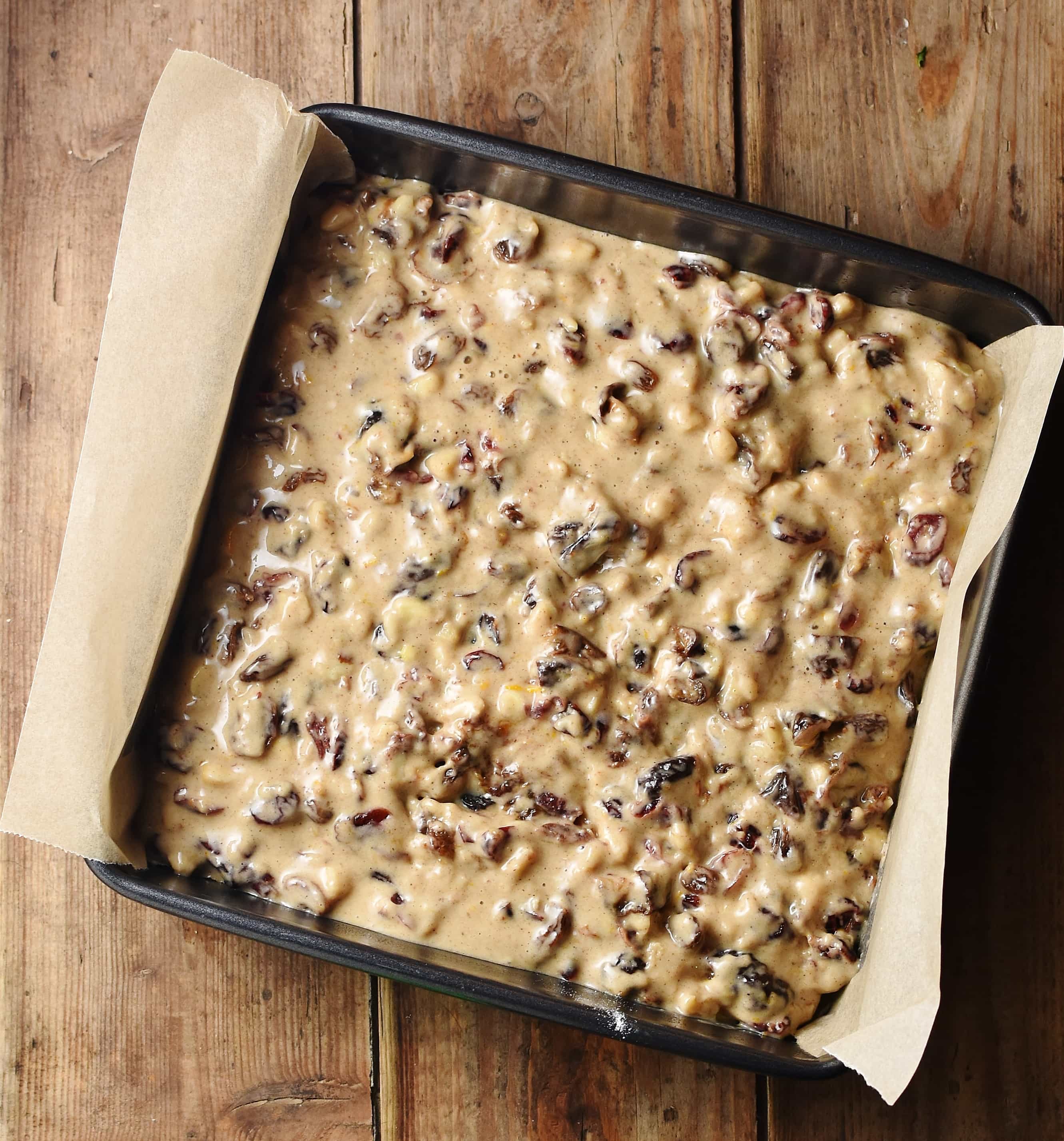Unbaked fruit cake in square cake pan lined with parchment paper.