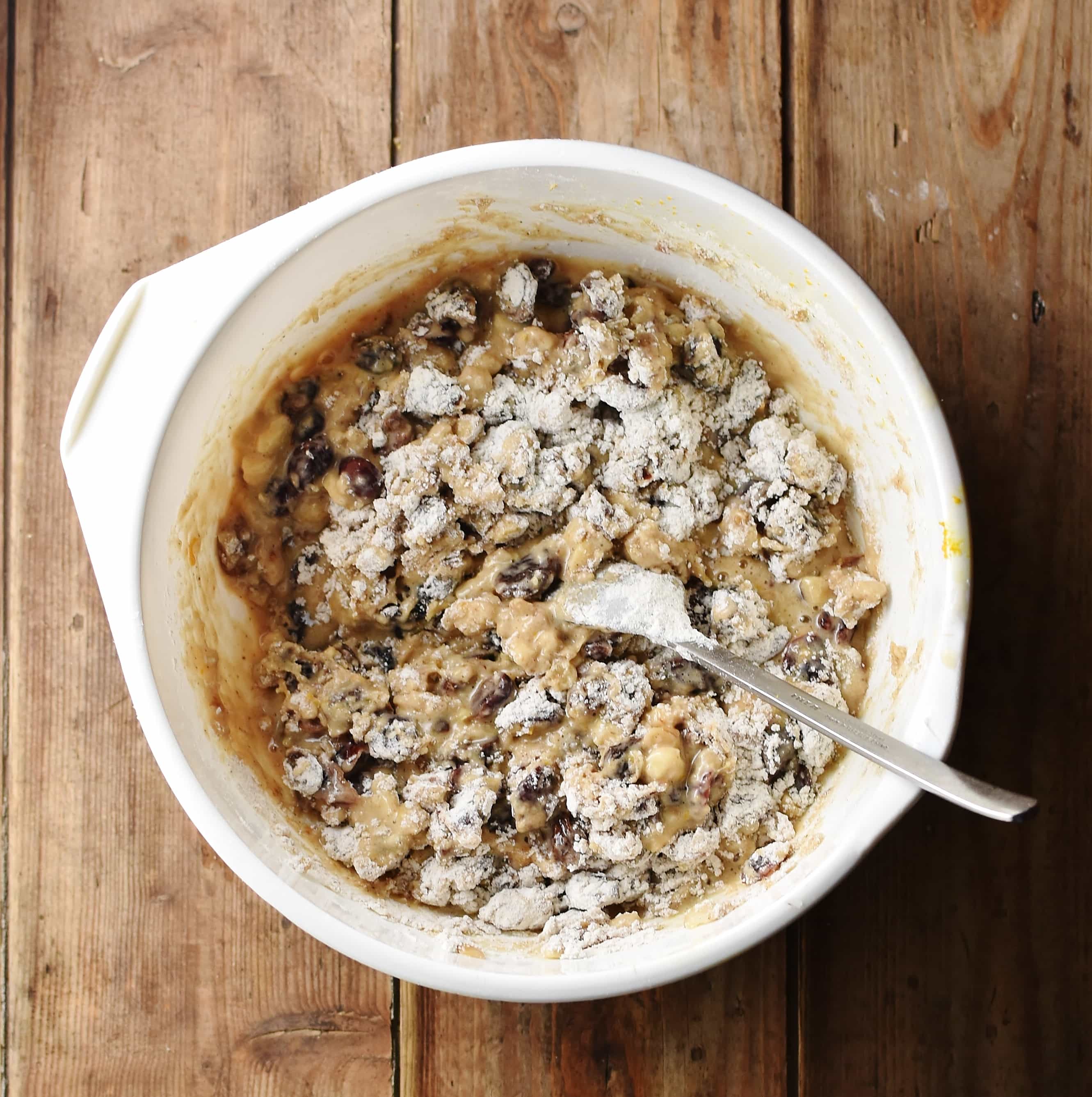 Fruit cake batter with some flour visible in white bowl with spoon.