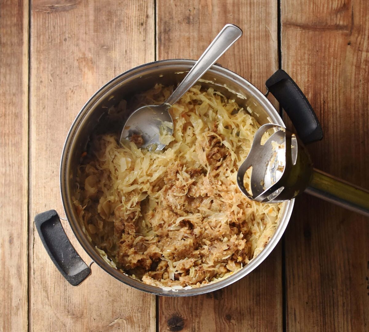 Cooked sauerkraut in pot with spoon and end of hand blender.