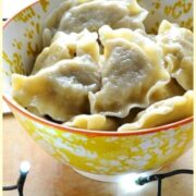 Sauerkraut pierogi in white-and-yellow patterned bowl with Christmas lights and green cloth in background.