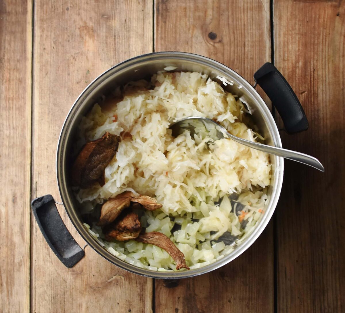 Sauerkraut and dried mushrooms in pot with spoon.